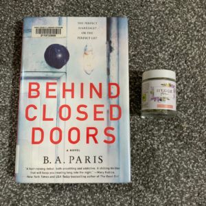 A hard cover copy of Behind Closed Doors by B.A. Paris next to a 1/8th jar of Hygge Farms cannabis